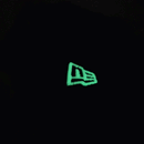 A glowing New Era logo stands out against a deep black backdrop, lit up in green while the surrounding image stays dark—mirroring the unique aesthetic of the chainstitch embroidery found on the San Francisco Giants All-Star Trolley Corduroy 19Twenty Snapback Hat in black and orange.