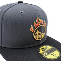 Graphite and black Golden State Warriors On Fire 59Fifty Fitted Hat featuring a yellow and red flame-encircled bridge logo on the front and a circular size sticker on the flat brim.