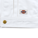 Close-up of the Selvedge Pleated Denim Jacket in white, featuring a gold button and logo patch sewn near the hem. The diagonal weave adds classic style and durability to this workwear-inspired piece.