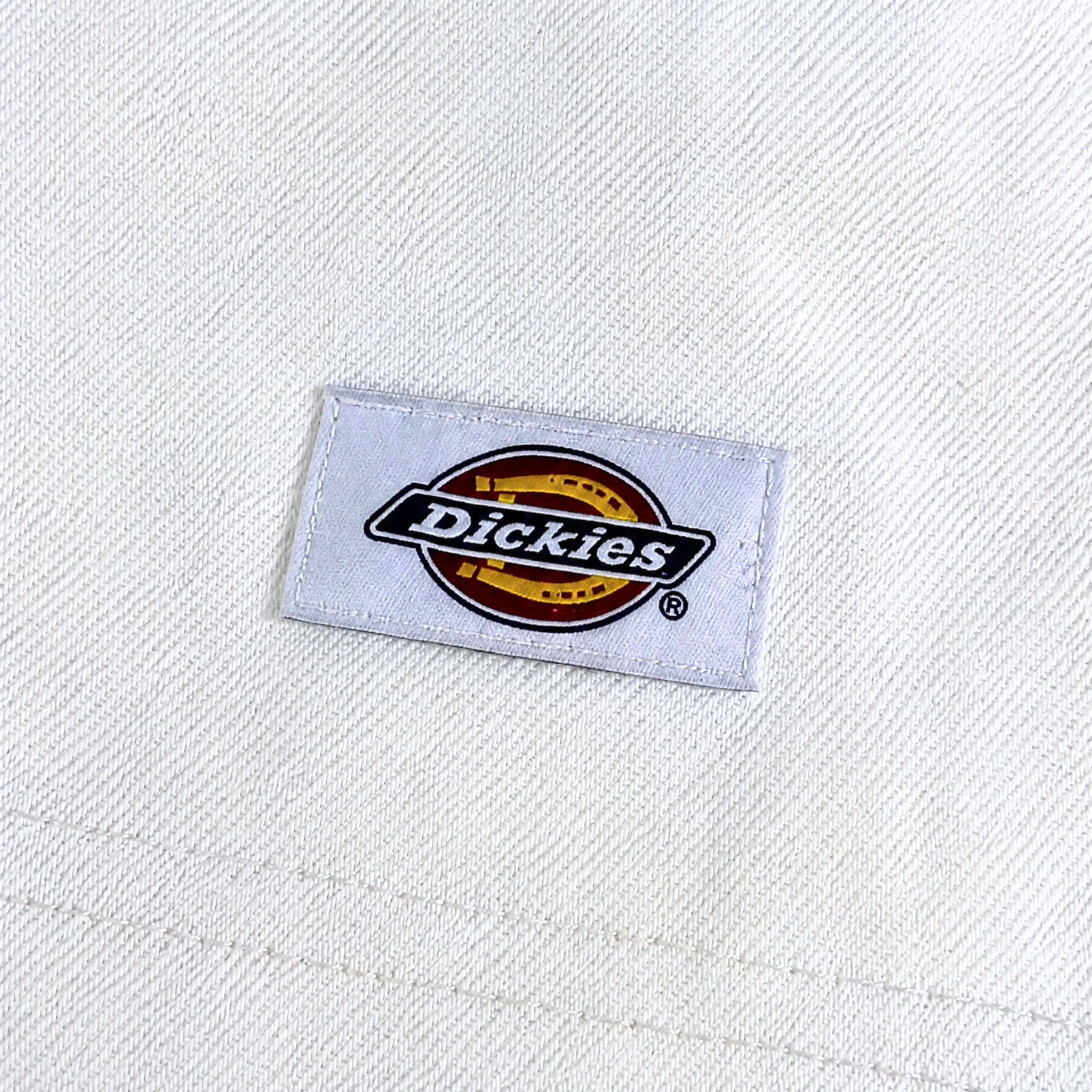A white fabric patch with the Dickies logo—black and white lettering on a red and yellow circle—sewn onto off-white textured fabric, ideal for pairing with the Selvedge Double Knee Denim Jeans in white.