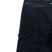 Close-up of Double Knee Canvas Shorts in black, featuring workwear-inspired design with a large front pocket, visible stitching, silver rivets, and a left-side belt loop.