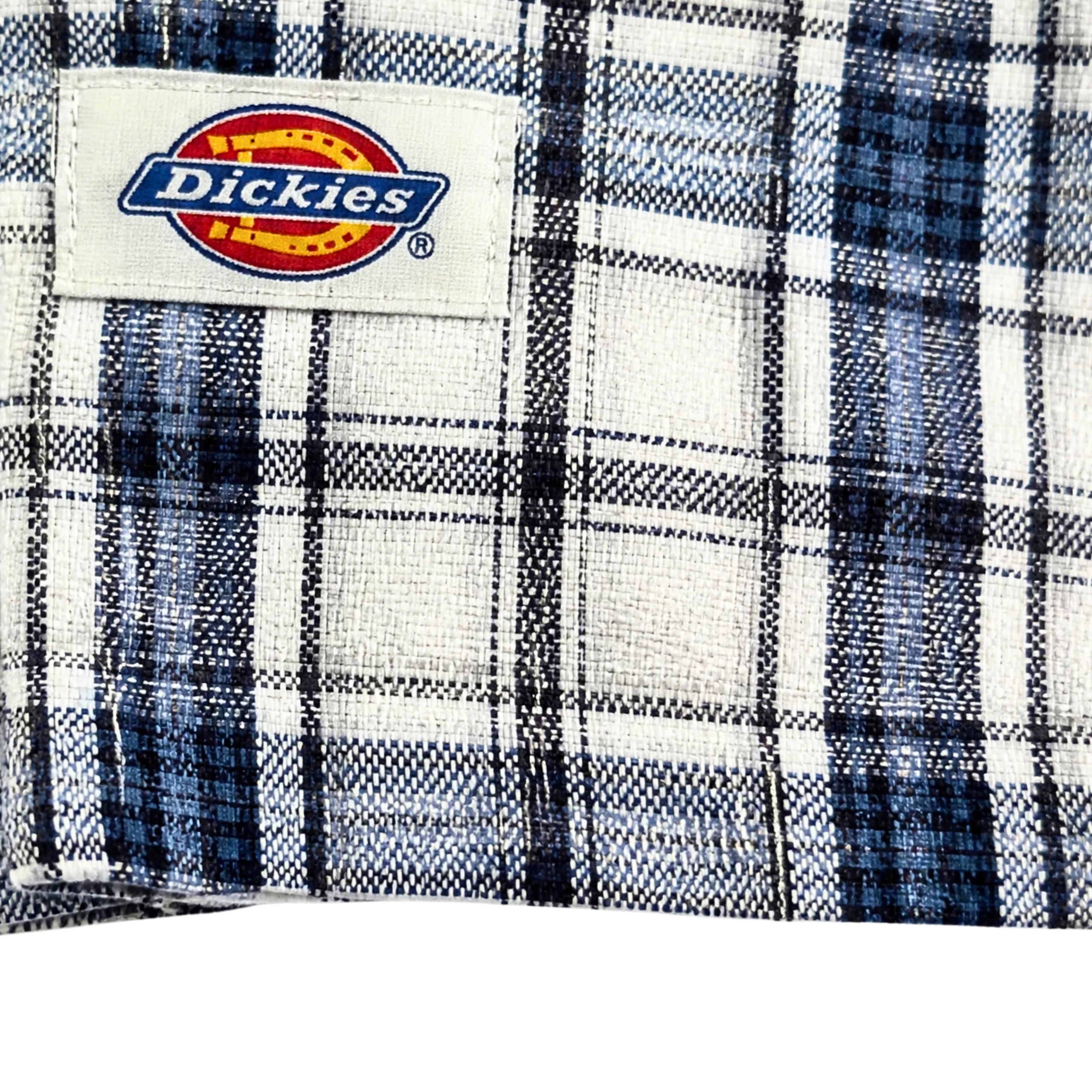 Close-up of the Springdale Short-sleeve Button-up Shirt in egret and blue, featuring a plaid cotton-linen blend and a sewn-on Dickies label with yellow, red, and blue logo. Perfect details on this stylish shirt.