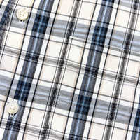 Close-up of the Springdale Short-sleeve Button-up Shirt in egret and blue, showing plaid cotton-linen fabric with intersecting black, blue, and gray lines on beige and two white buttons—a classic short-sleeve style.