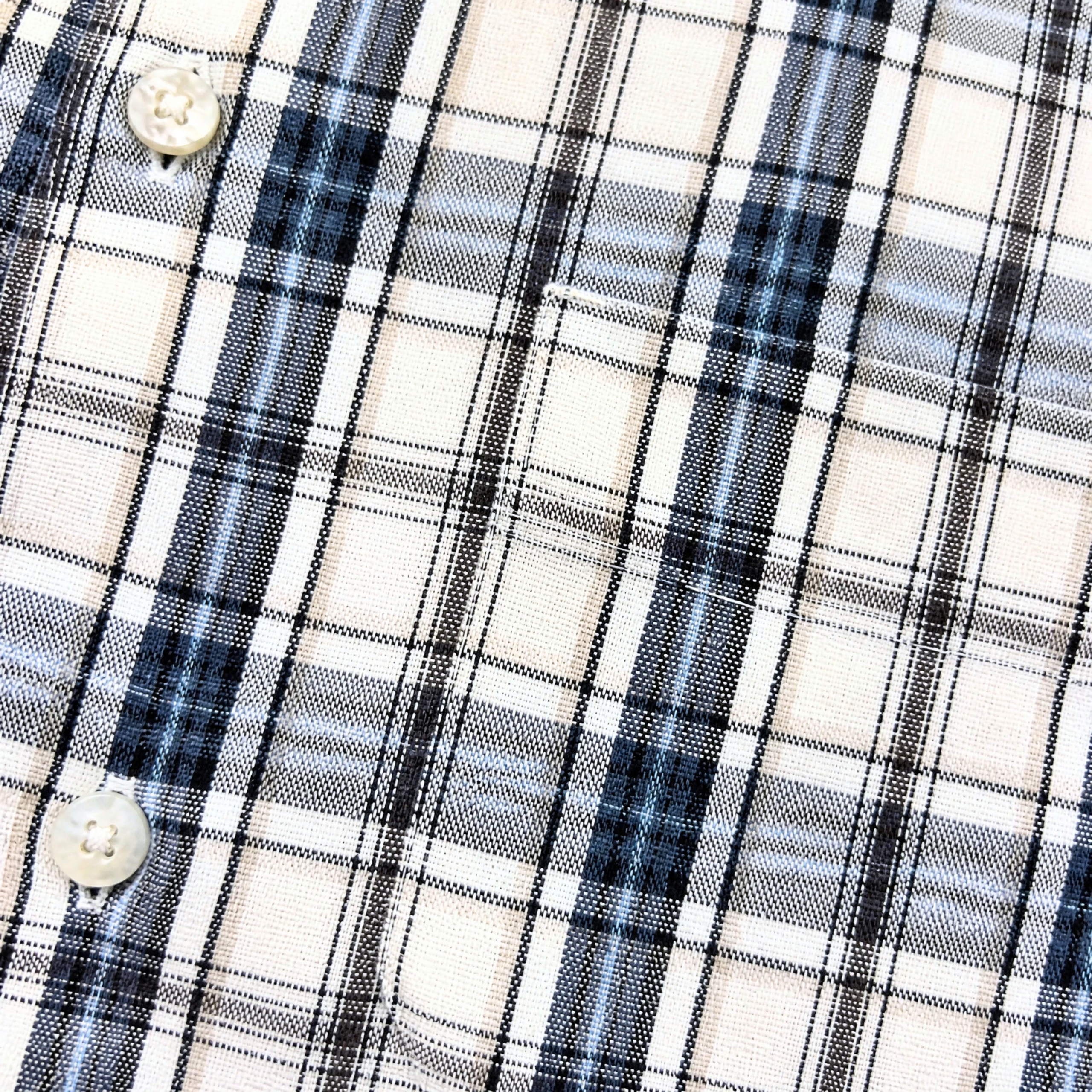 Close-up of the Springdale Short-sleeve Button-up Shirt in egret and blue, showing plaid cotton-linen fabric with intersecting black, blue, and gray lines on beige and two white buttons—a classic short-sleeve style.