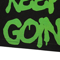 Close-up of green, graffiti-style text on black shows "KEEP GOIN'"—perfect for the Keep Goin' Tee in black, an oversized streetwear piece inspired by San Francisco's Mission District energy.