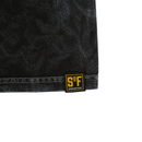 Close-up of heavyweight cotton fabric from the Just Relax Tee in mineral black, featuring a visible seam and a small black and yellow patch near the edge with "S F" and "STATE OF FLUX.