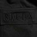 Close-up of black fabric on the Flux Utility Cargo Pants in black, featuring "STATE OF FLUX" embroidered in matching black thread for a subtle, textured effect. The embroidery appears on a rectangular patch stitched onto the pants, echoing the signature detailing found on premium cargo pants with utility pockets.