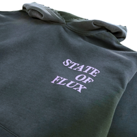 A heavyweight hoodie in distressed faded black and lilac with the words STATE OF FLUX printed in bold, light-colored letters on the chest.