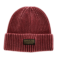 Introducing the Ribbed Knit Mantra Beanie in washed burgundy—a cozy red beanie crafted from a soft rayon blend, featuring a folded brim and a rectangular patch that displays “STATE OF FLUX” alongside an inspiring motivational quote in smaller lettering.