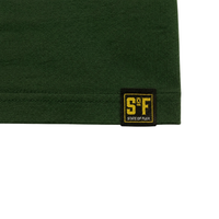 A close-up of the forest green fabric from the Answer The Call Tee, a heavyweight oversized piece featuring a black and yellow State of Flux tag stitched near the hem—perfect for streetwear layering.