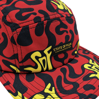 A close-up of the Zippered Psycapdelic 5-Panel Hat in blood red and bright yellow, featuring a bold pattern and a STATE OF FLUX SAN FRANCISCO USA label on the front panel. This stylish stretch fabric cap offers comfort while making a vivid statement.