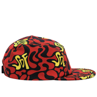 The Zippered Psycapdelic 5-Panel Hat in blood red and bright yellow is crafted from stretch fabric, featuring an abstract squiggle pattern, yellow SDF text, and a red-and-black design, shown here from the side.