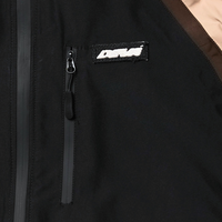 Close-up of a black Disorder Shell Jacket with a zippered chest pocket and a rectangular embroidered patch.