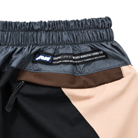Close-up of Disorder Track Pants in black and beige featuring a black, brown, and beige color-blocked design with an elastic waistband and a rectangular label that reads GRAPHIC [グラフ] WEARS MANUFACTURING CO.